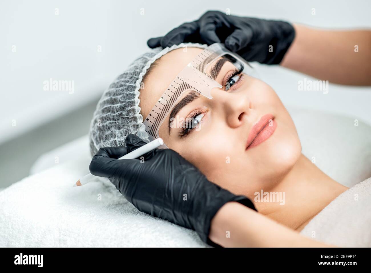 Markup mit Lineal auf Augenbrauen der jungen Frau während der dauerhaften Make-up. Stockfoto