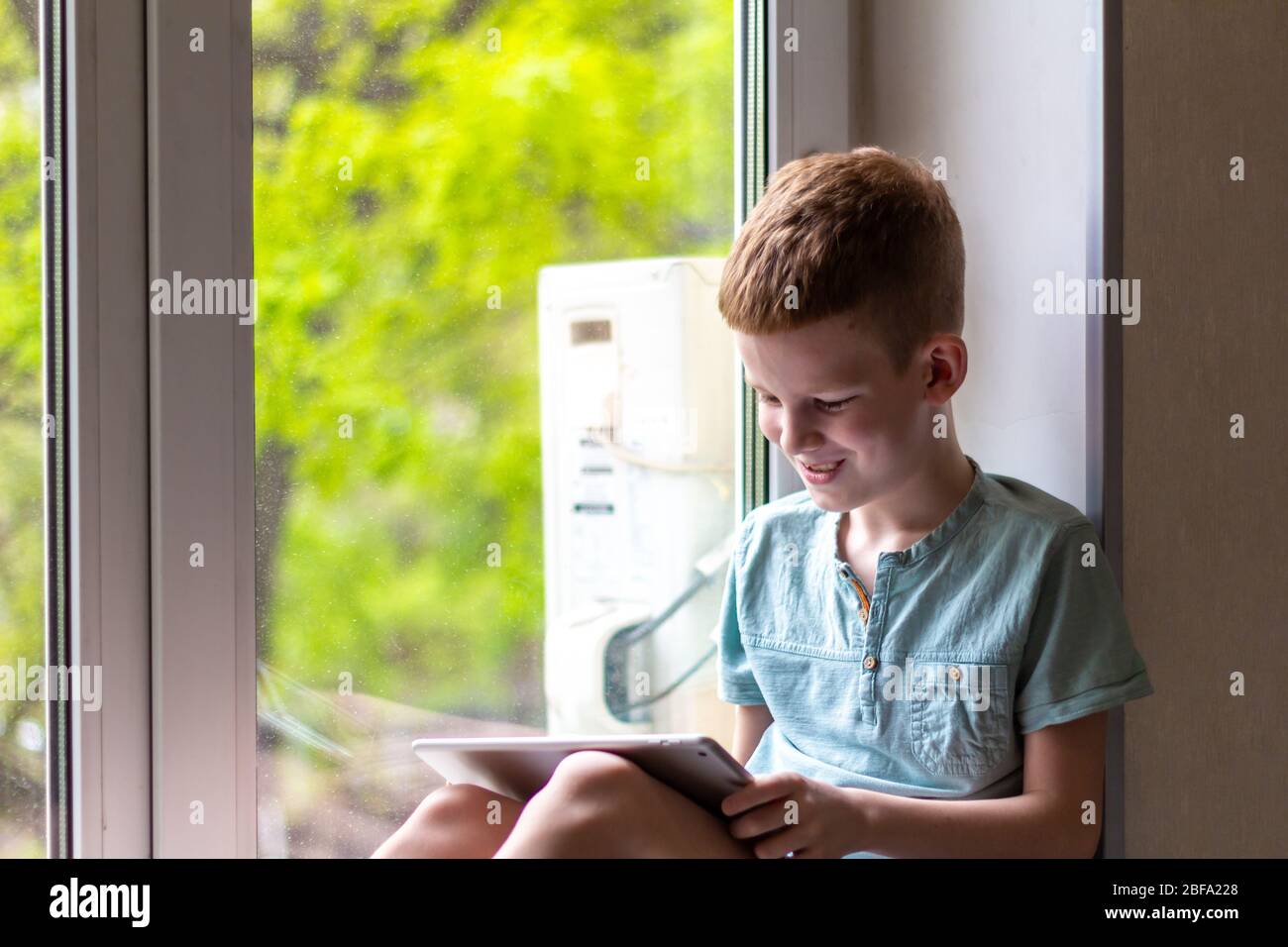 Junge sitzen auf Fensterbank mit Tablet und spielen die Spiele. Während der Quarantäne zu Hause bleiben. Stockfoto