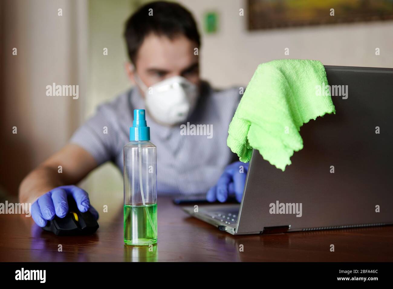 Ein Mann in einer Schutzmaske und medizinischen Handschuhen sitzt an einem Laptop und arbeitet aus der Ferne. Home Office. Konzept der Hygiene und Sauberkeit während der Stockfoto