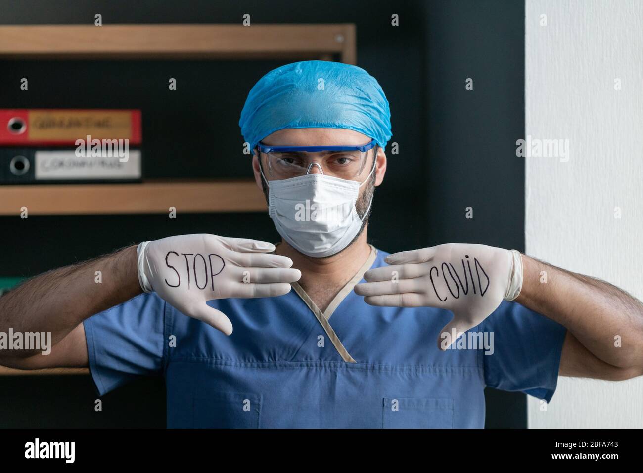 Mann In Blauer Medizinischer Uniform Zeigt Slogan, Covid Zu Stoppen Stockfoto