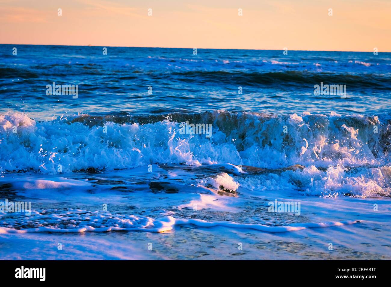 Toller Sonnenuntergang am Strand mit unglaublich glitzernden Wellen. Sonnenuntergang und Wellen am spektakulären Strand. Blau und Gelb unendlich Stockfoto