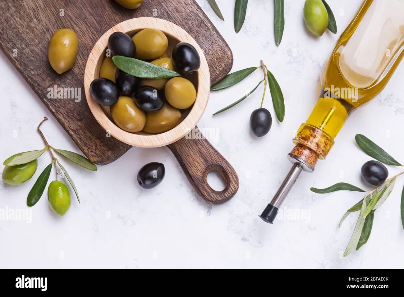 Schwarze und grüne Oliven in Holzschale und Ölflasche auf weißem Marmortisch, Stockfoto