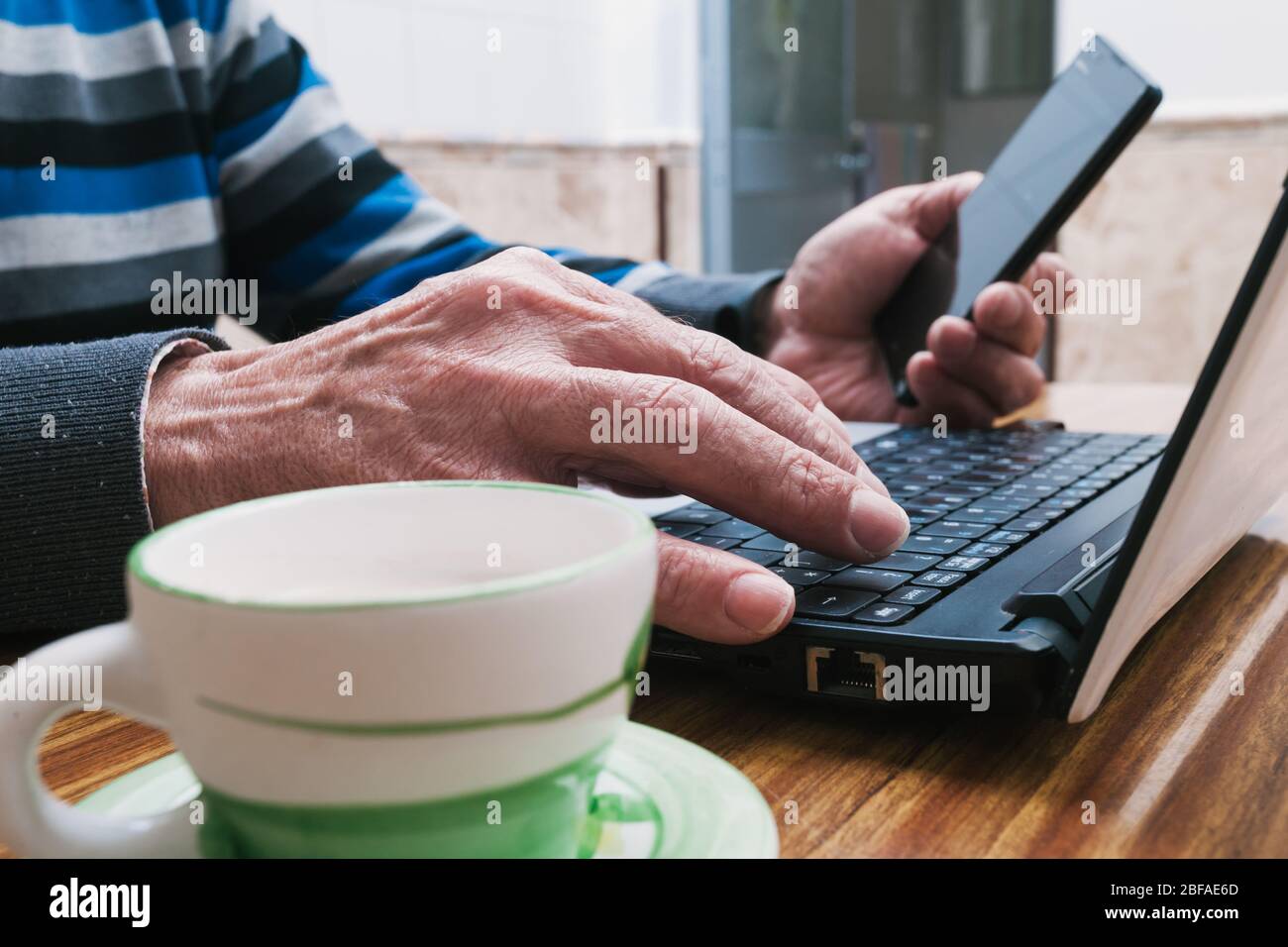 Älterer Mann, der Laptop tippt und das Handy zu Hause benutzt. Telearbeit während der Haft. Kommunikation mit Familienangehörigen während der Quarantäne. Sel Stockfoto