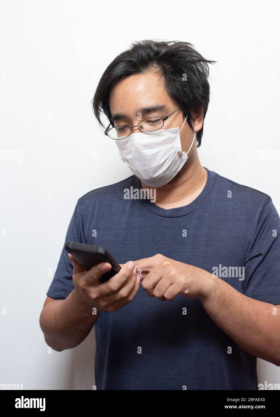 Asiatischer junger Mann in lässig tragen chirurgische medizinische Maske COVID-19 mit Smartphone auf weiß isoliert schützen Health Care Konzept.Wuhan coron Stockfoto