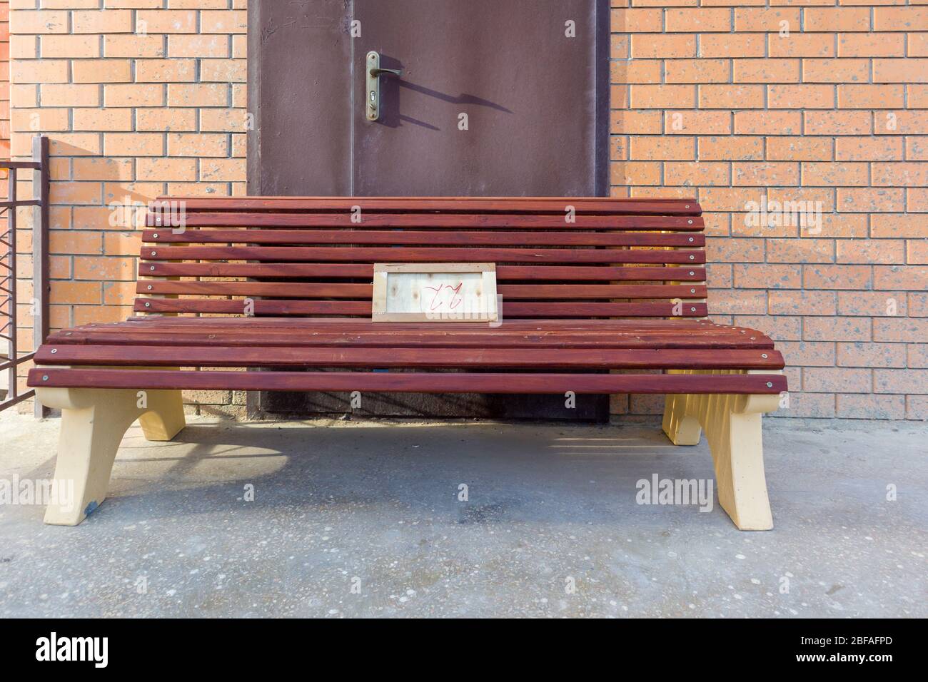 Eine Holzbank, die vor der Tür in einem Backsteingebäude sitzt. Stockfoto