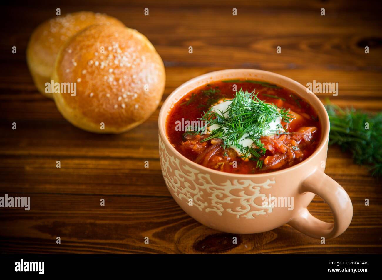 Heiße Rote-Bete-Suppe mit Sauerrahm, Kräutern und Brötchen in einer ...