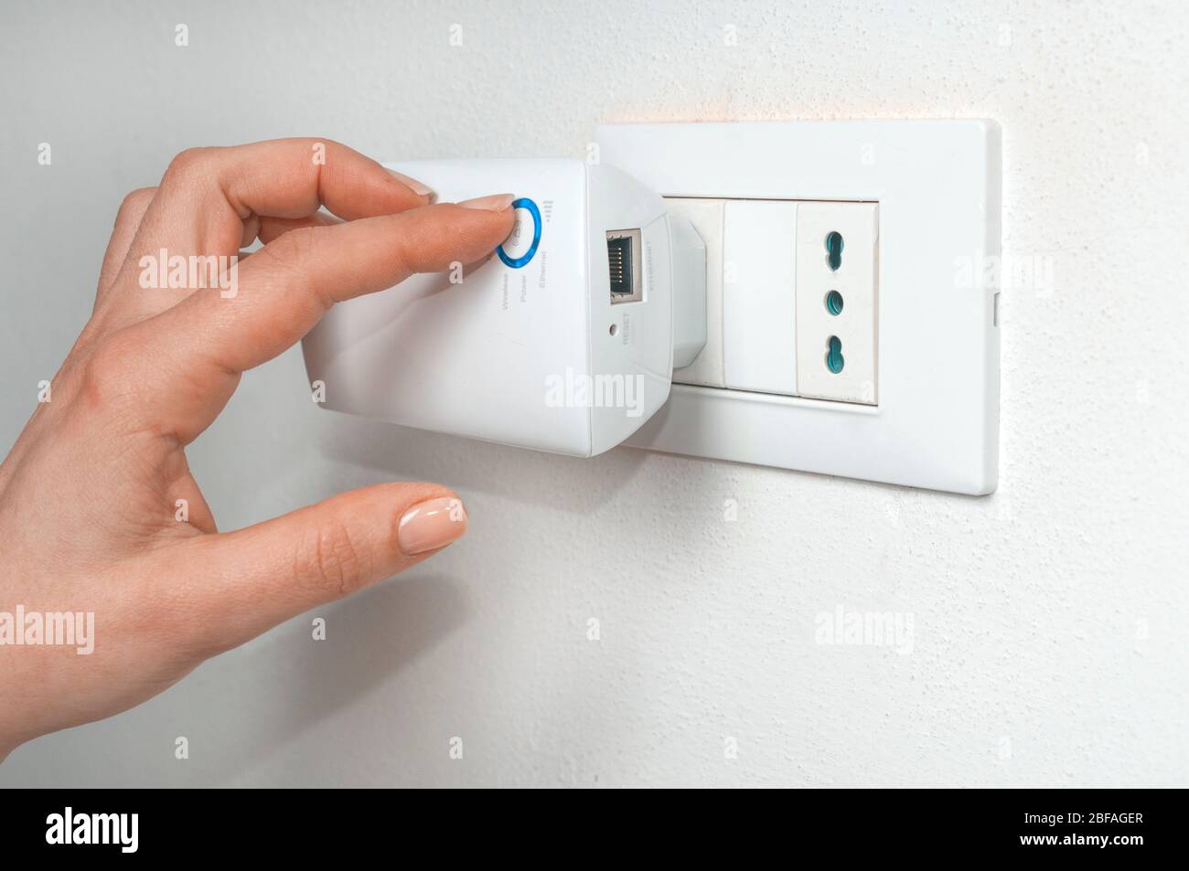Frau schalten Sie einen WLAN-Repeater an einem Wandstecker angeschlossen Stockfoto