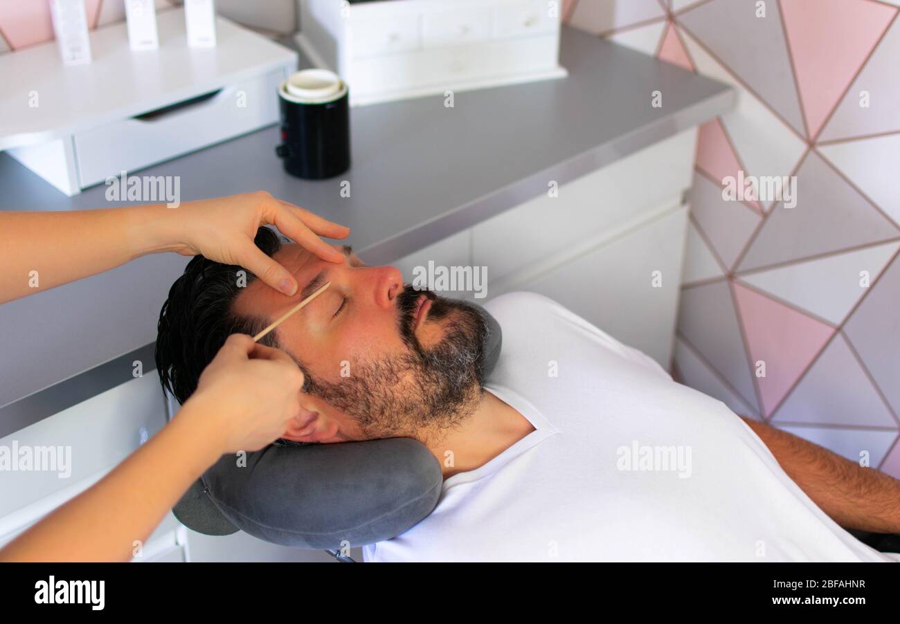 Weißer Mann mit dunklem Haar und Bart genießt Schönheitsbehandlungen. Männliche Pflegebehandlungen einschließlich Wachsen, Färben und Haarentfernung. Stockfoto