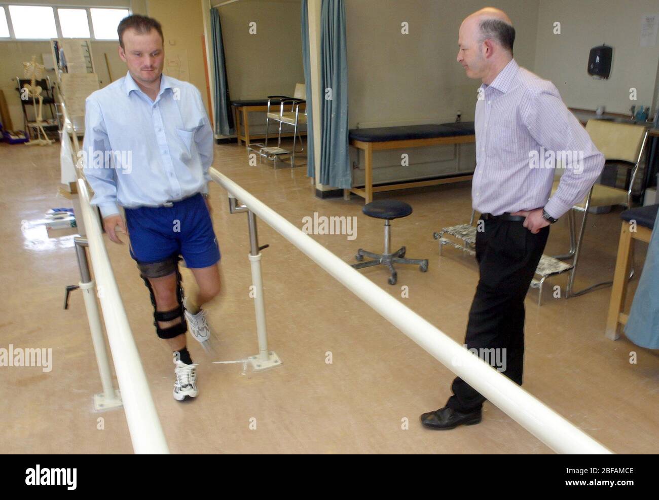Von einem Techniker beobachtet, ein männlicher Patient mit einem rechten Bein Donjoy Prothese ausgestattet Gehen mit der Unterstützung einer Handschiene. Stockfoto
