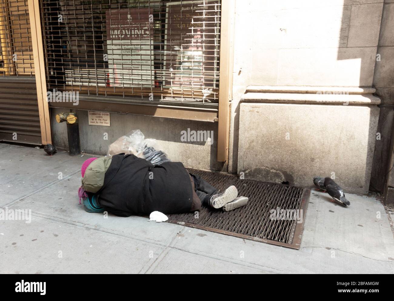 Obdachlose Person, die auf einem Gitter in der 57. Straße in Manhattan schläft. Tauben werden gesehen, die um die Person herumwandern, ein Symbol der Einkommensungleichheit Stockfoto