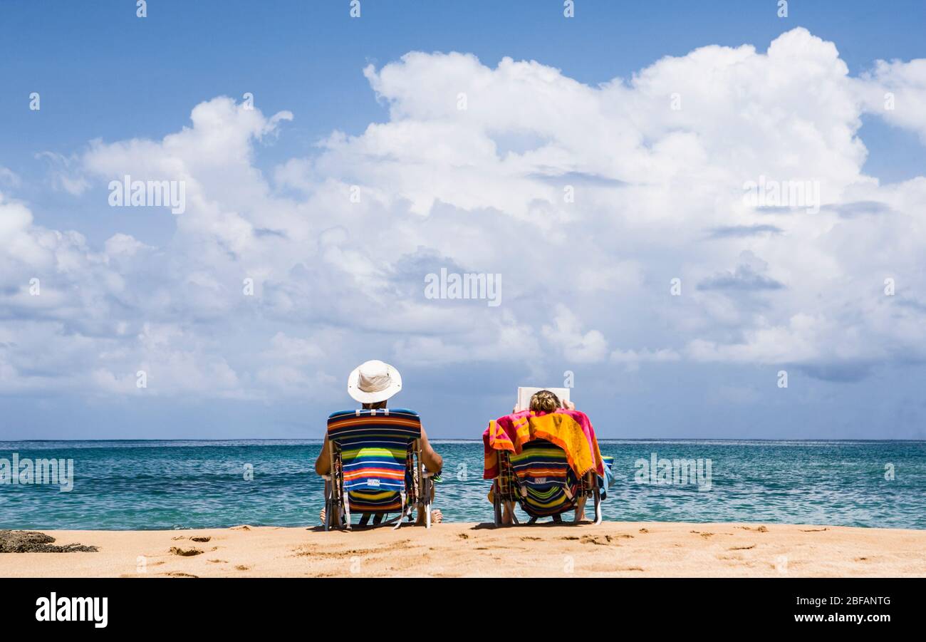 Ein Paar sitzt auf einem Strand in ihren Stühlen und entspannt sich in der Sonne. Moloa a Bay Beach, Kauai, Hawaii, USA. Stockfoto