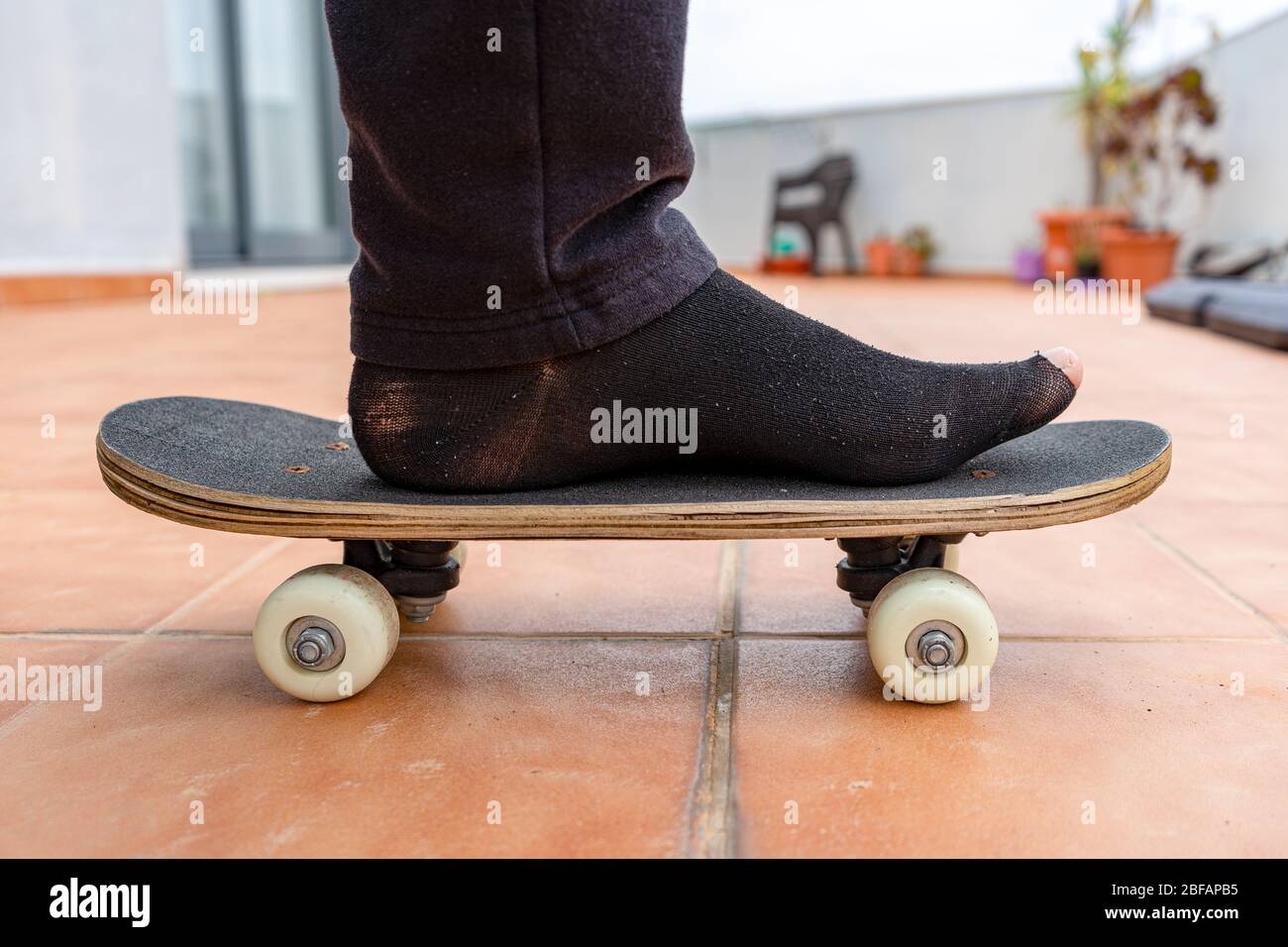 Mann in schwarzen Socken mit Löchern auf einem Skateboard auf der Terrasse seines Hauses. Spaßkonzept Stockfoto