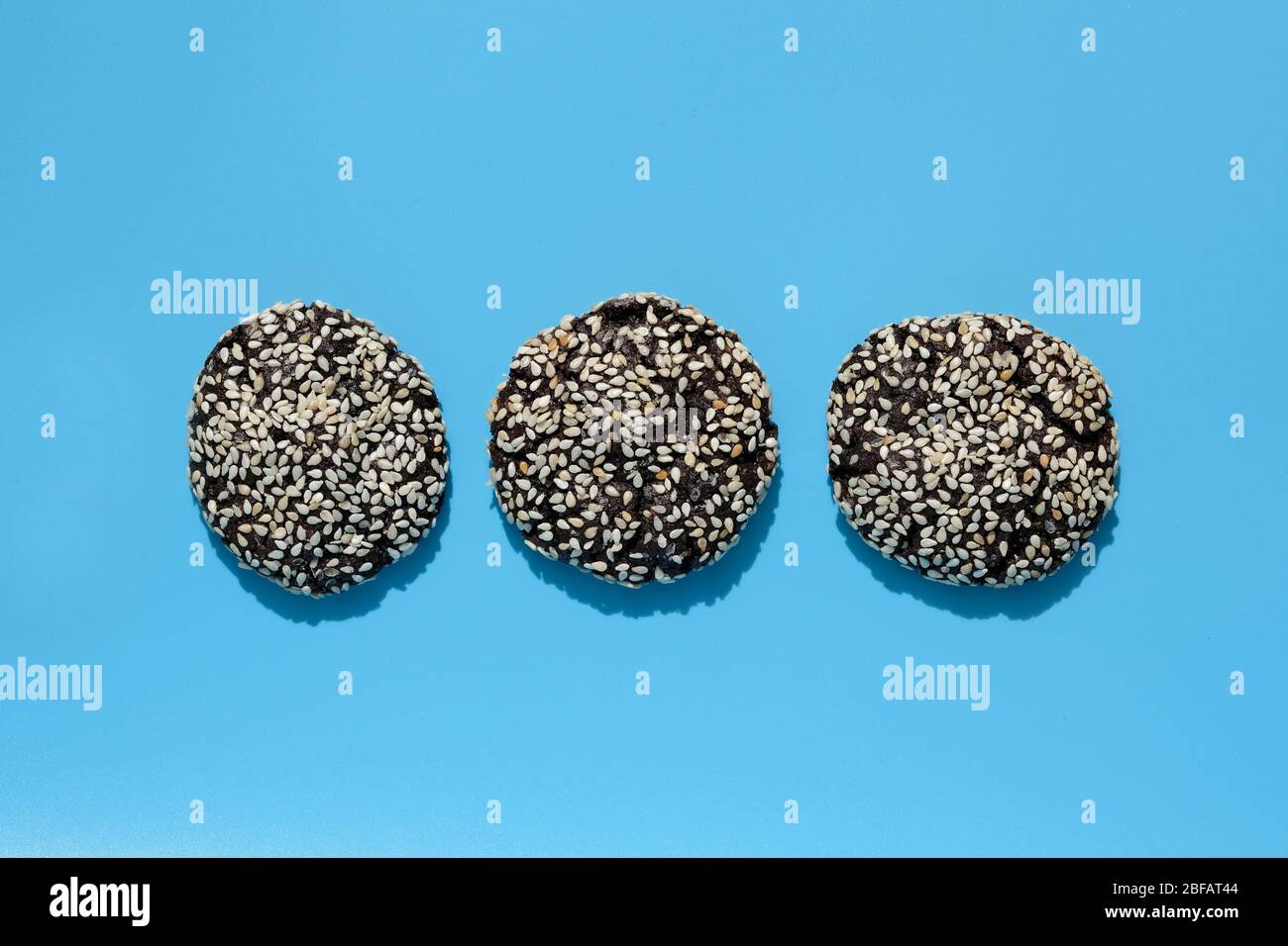 Drei Schokoladenkekse mit Sesamsamen auf der Oberseite. Runde Schokoladenkekse auf blauem Hintergrund. Leckere Plätzchen Hintergrund. Stockfoto