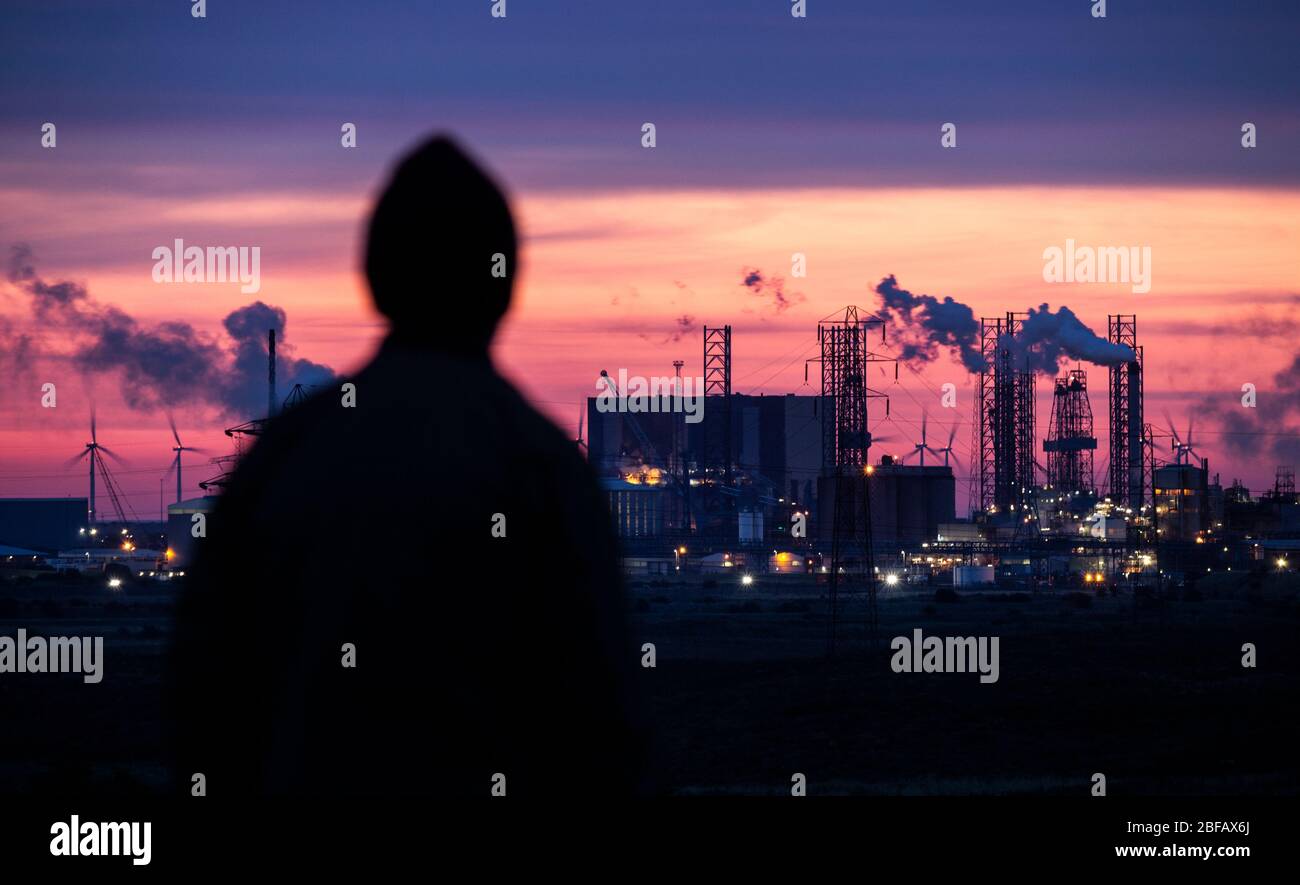 Mann, der bei Sonnenaufgang auf den Schwerindustriekomplex schaut. Luftverschmutzung in Verbindung mit schwereren psychischen Erkrankungen. Depression, Klimawandel.. Konzept Stockfoto