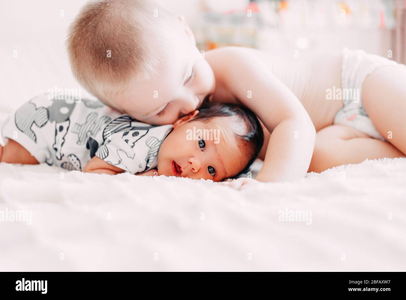 Ältere Bruder blonde Haare Kuss Baby Schwester liegen auf dem Bett zu Hause Liebe Familie Konzept Stockfoto