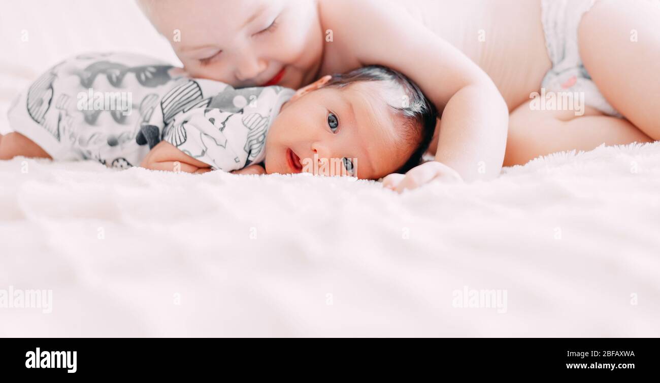 Ältere Bruder blonde Haare Kuss Baby Schwester liegen auf dem Bett zu Hause Liebe Familie Konzept, Banner Stockfoto
