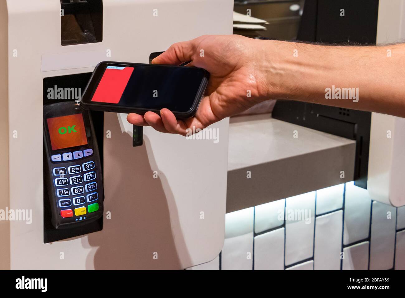 Ein Kunde, der einen NFC-Kontakt abgibt, zahlt mit seinem Handy in einem Fast-Food-Restaurant weniger Stockfoto