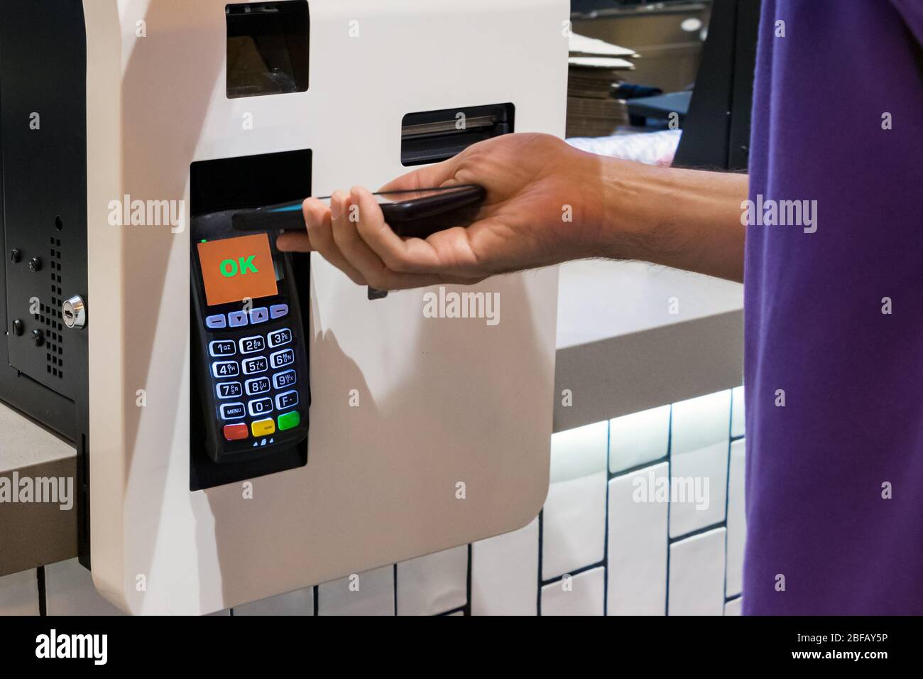 Ein Kunde, der einen NFC-Kontakt abgibt, zahlt mit seinem Handy in einem Fast-Food-Restaurant weniger Stockfoto