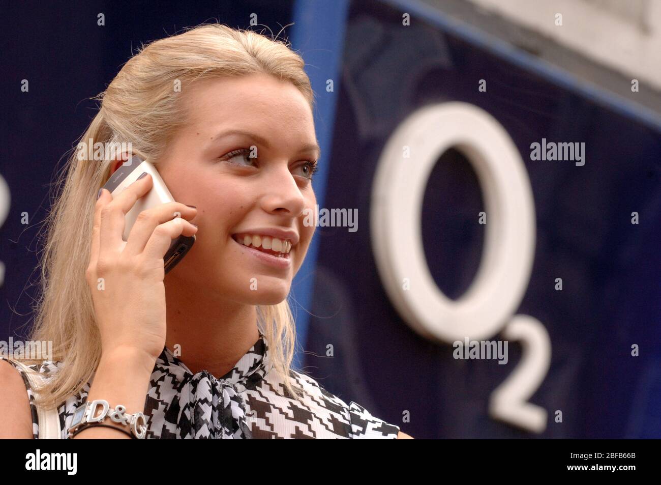 Junge Frau am Handy vor einem O2-Laden. Stockfoto