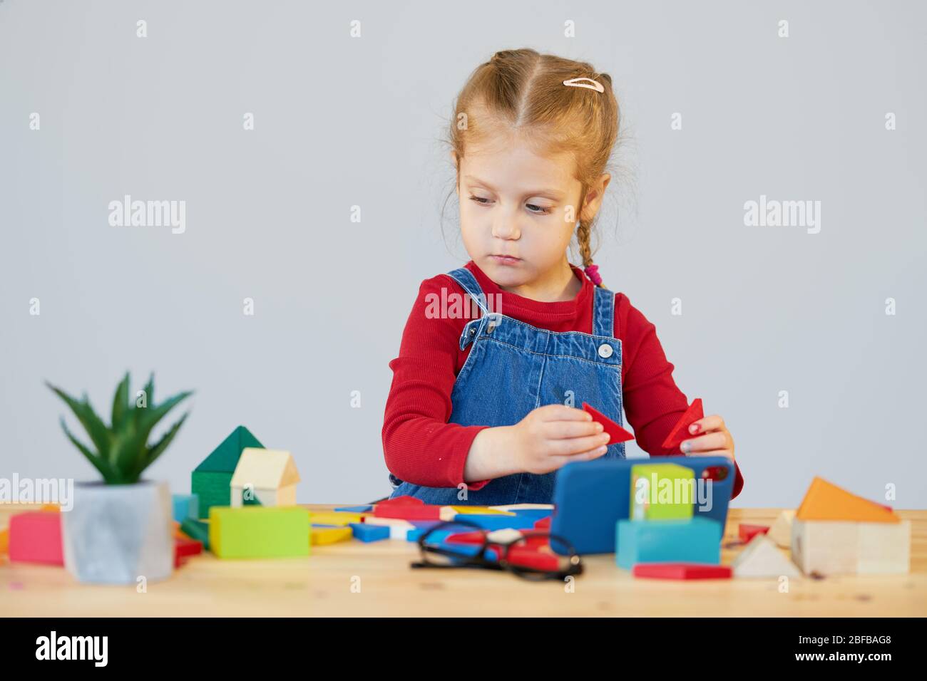 Online Fernstudium zu Hause während der Quarantäne. Ein intelligentes Kind mit Brille sammelt einen mehrfarbigen Konstruktor an einem Tisch im Klassenzimmer. Stockfoto