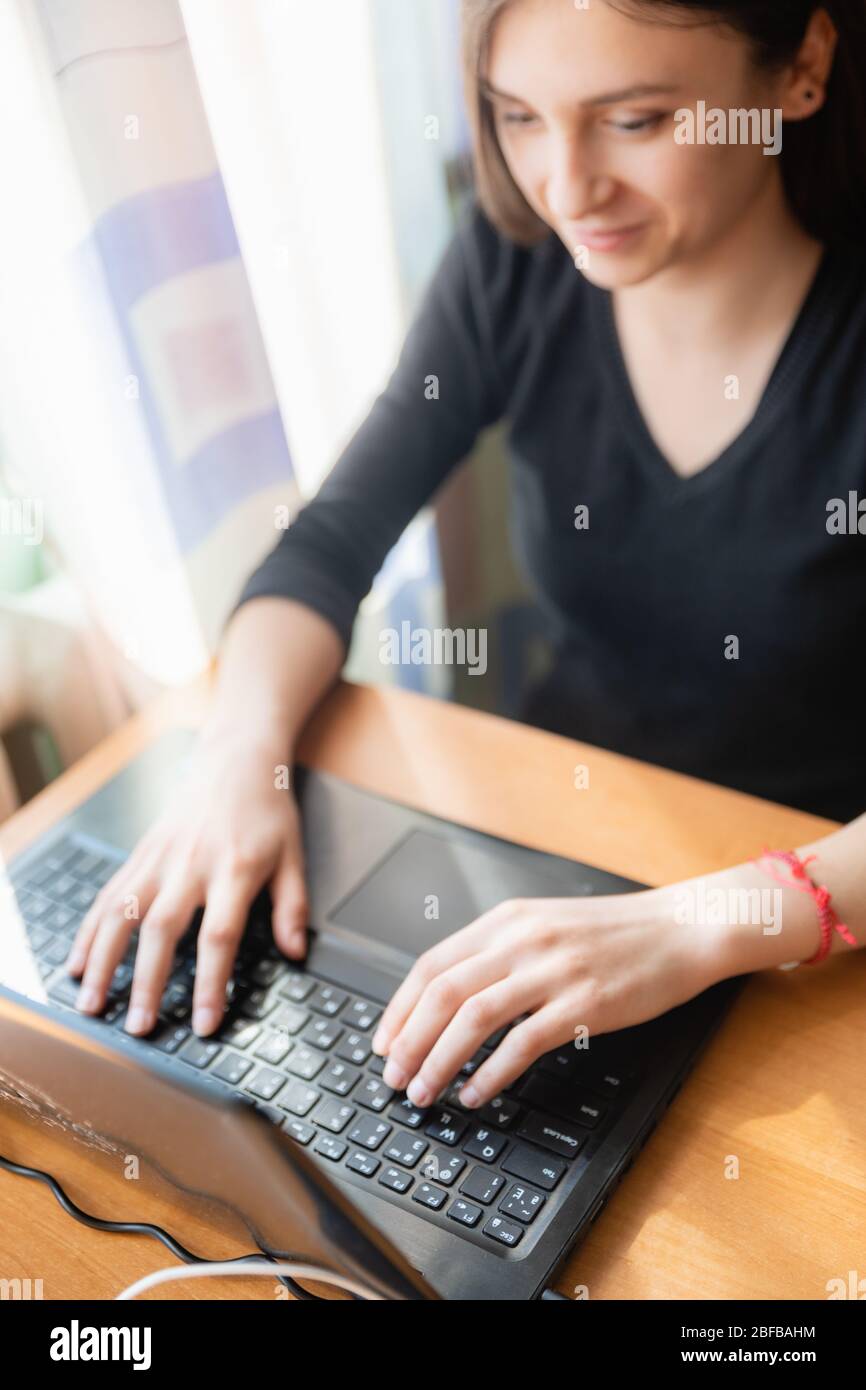 Junge kaukasische Mädchen in schwarzen Pullover Blick auf Computer beim Online-Studium zu Hause in der Nähe des Fensters Stockfoto