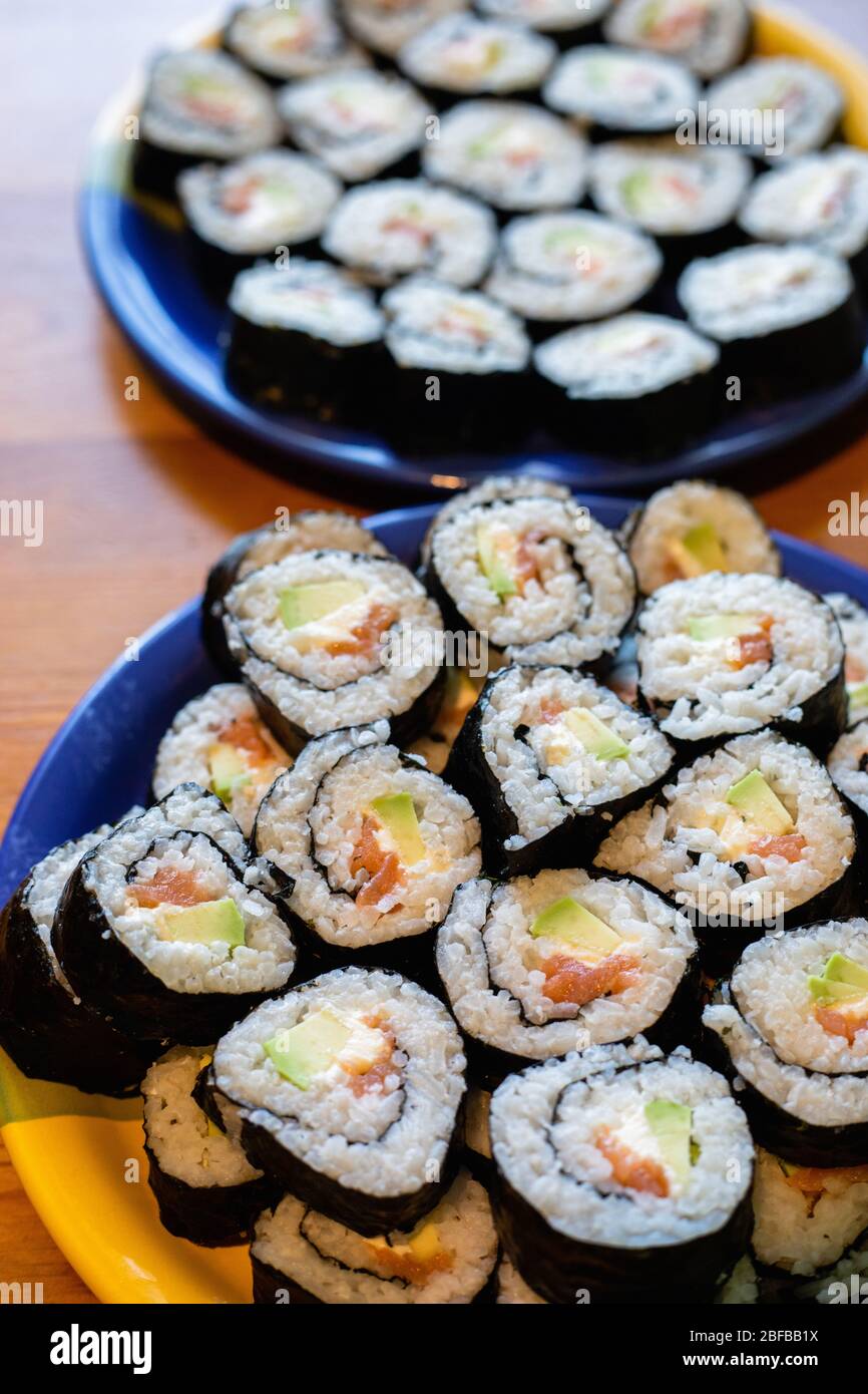 Zwei runde Teller mit hausgemachtem Sushi Maki mit Lachs, Reis und Avocado auf Holztisch Stockfoto