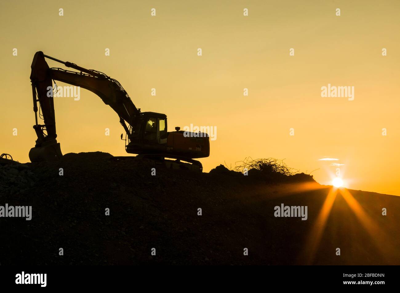 Baustellenidylle, Bagger auf Baustelle bei Sonnenuntergang mit Sonnenstein, Silhouette Stockfoto