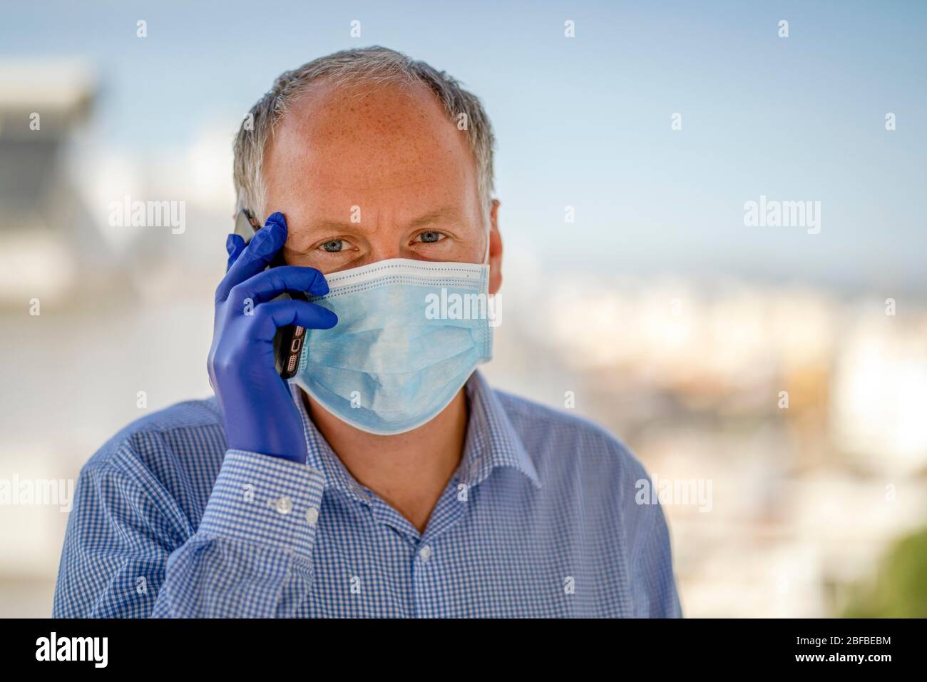 Mann mit Schutzmaske und blauen Latexhandschuhen während der Verwendung von Handy, Deutschland Stockfoto