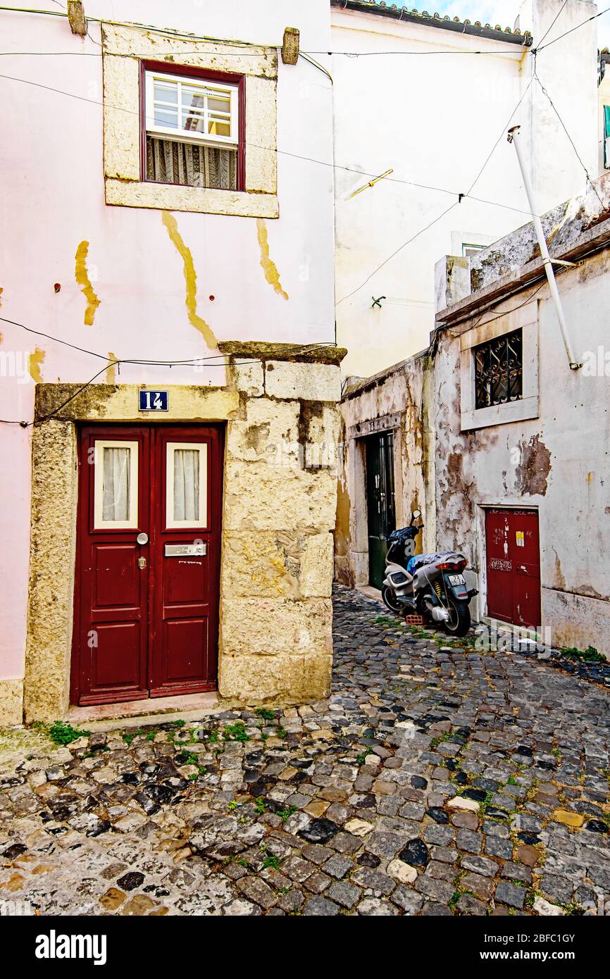 Kleine schiefe rote Tür und Motorrad auf einer schmalen Straße der Alfama in Lissabon Stockfoto