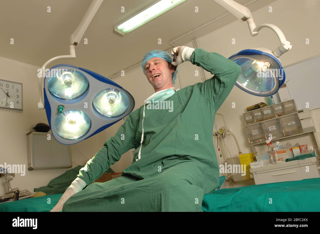 Chirurg sitzt auf Operationstisch, während er mit seinem Mobiltelefon spricht. Stockfoto