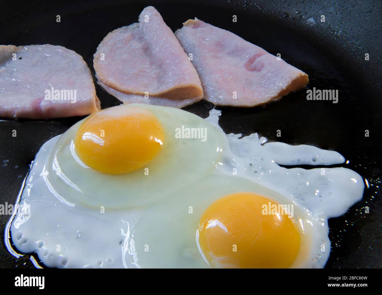 Zubereitung von überleichten Eiern und Schinken, auf einer Pfanne, als Teil des klassischen Frühstücks. Eier auf einem Topf-Konzept kochen. Stockfoto