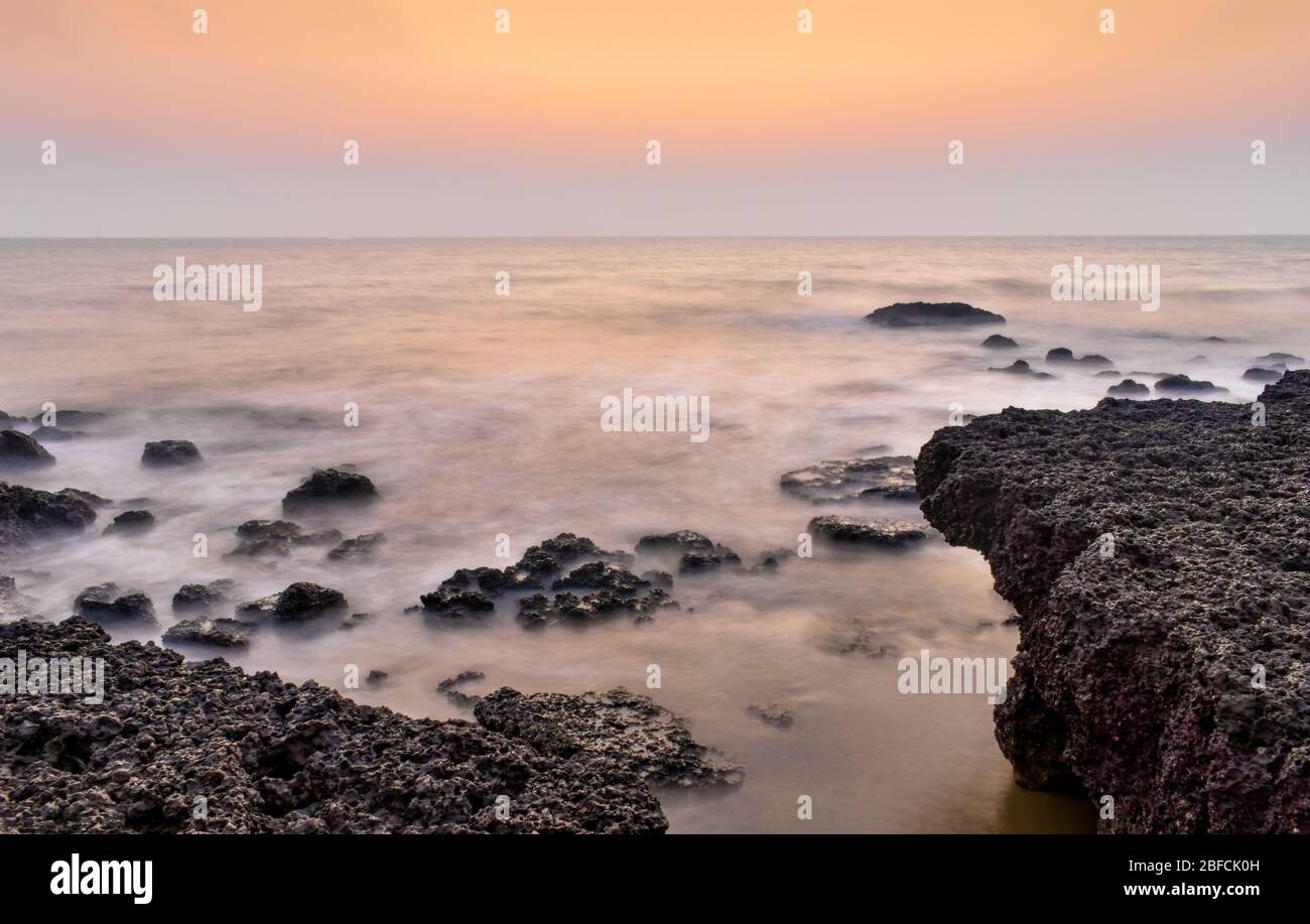 Erstaunliche Landschaft der Küsten-Ignous Felsen mit klarem sichtbaren Horizont bei Sonnenuntergang / Sonnenaufgang. Meereswellen, die die Felsen stürzen, werden durch die Exposition geglättet Stockfoto