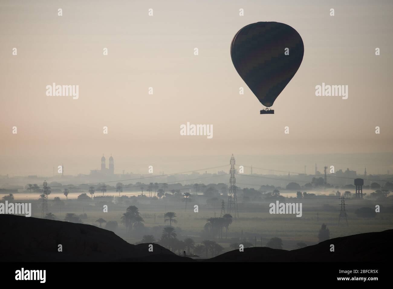 Heißluftballons, die über Luxor und der alten Stadt aufsteigen, wie vom Leichentempel der Hatschepsut am Westufer des Nils aus gesehen. Stockfoto