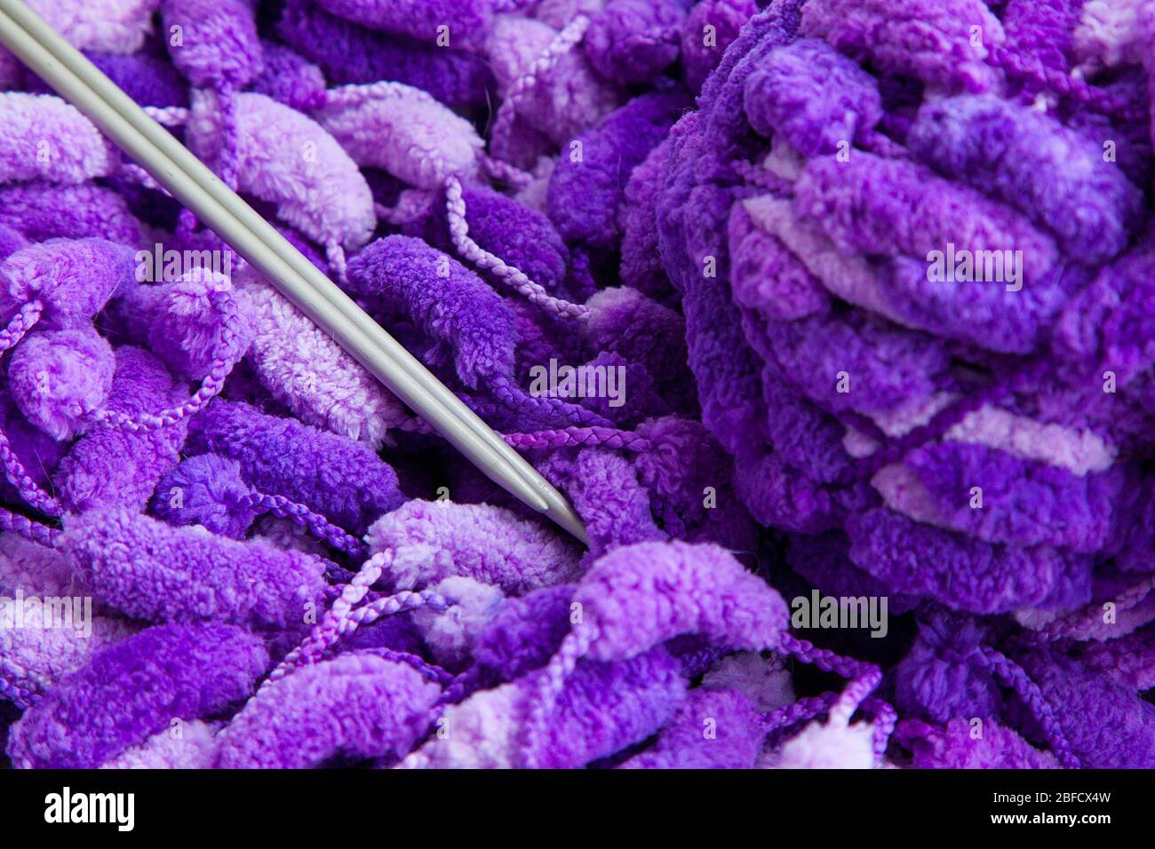 Ein Set von Handarbeiten zum Stricken. Nahaufnahme eines schönen lila-weißen Garns mit einem Ball und Speichen. Stockfoto