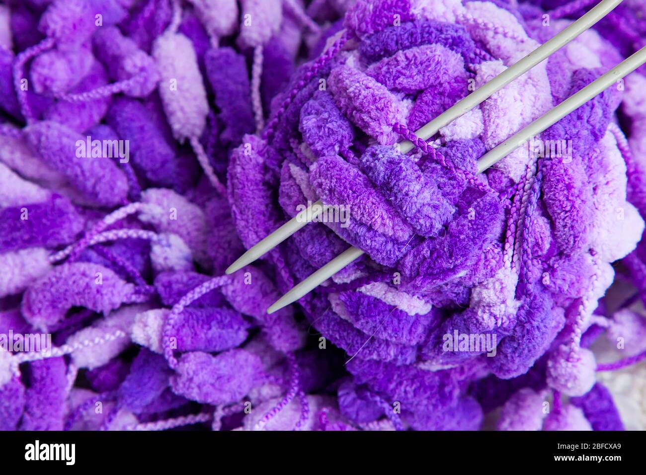 Ein Set von Handarbeiten zum Stricken. Nahaufnahme eines schönen lila-weißen Garns mit einem Ball und Speichen. Stockfoto