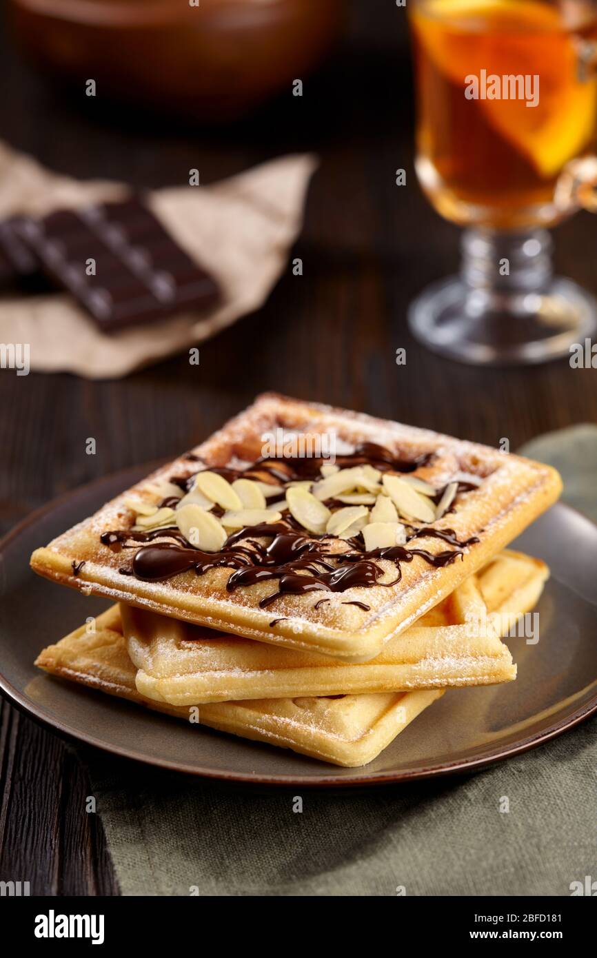 Wunderschönes Frühstück. Hausgemachte belgische Wiener Waffeln mit Schokolade und Erdbeeren, Tee auf dunklem Holzhintergrund dekoriert. Stockfoto