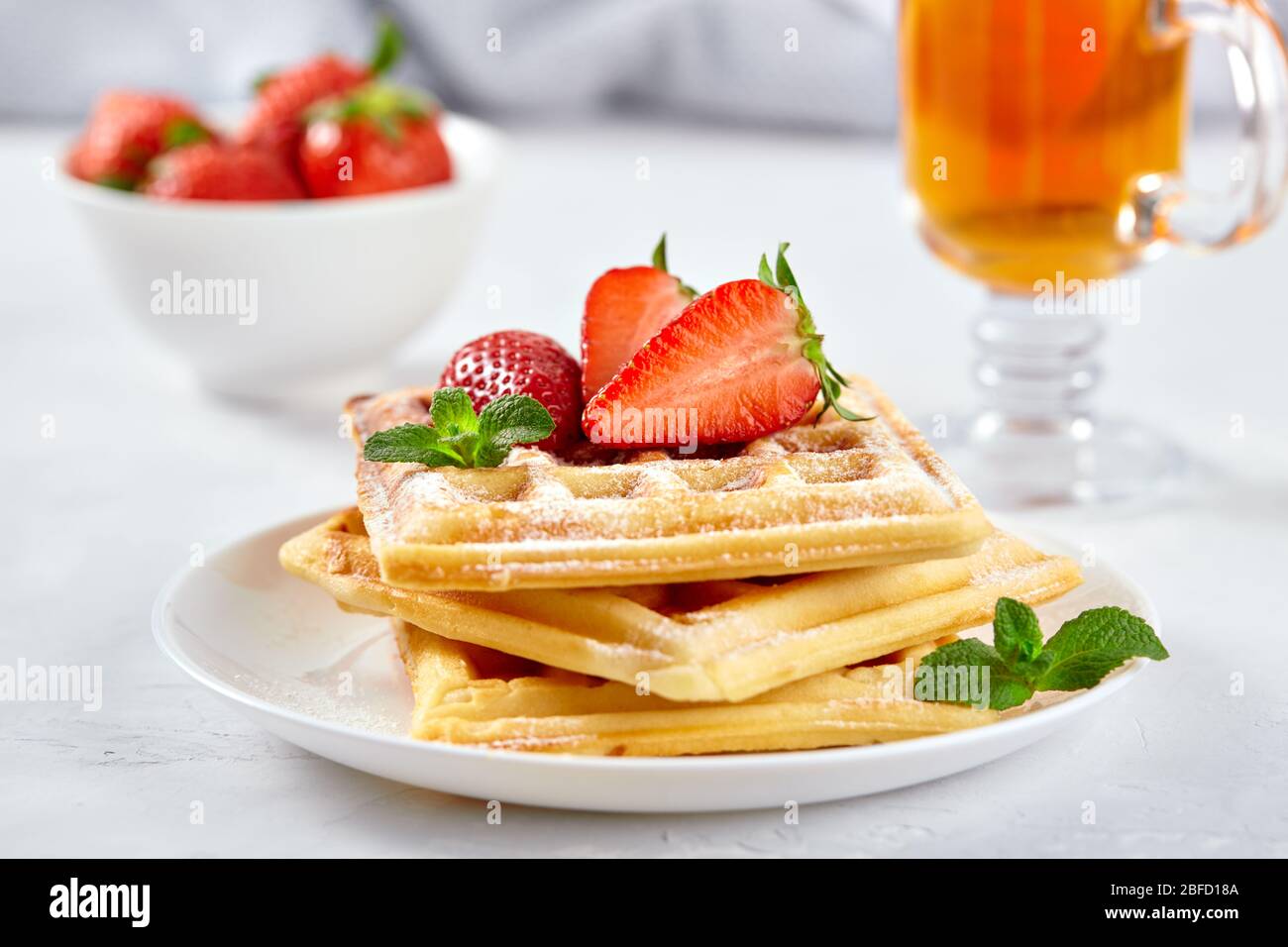 Wunderschönes Frühstück. Hausgemachte belgische Wiener Waffeln mit Erdbeeren, Tee auf einem hellen Hintergrund dekoriert. Stockfoto