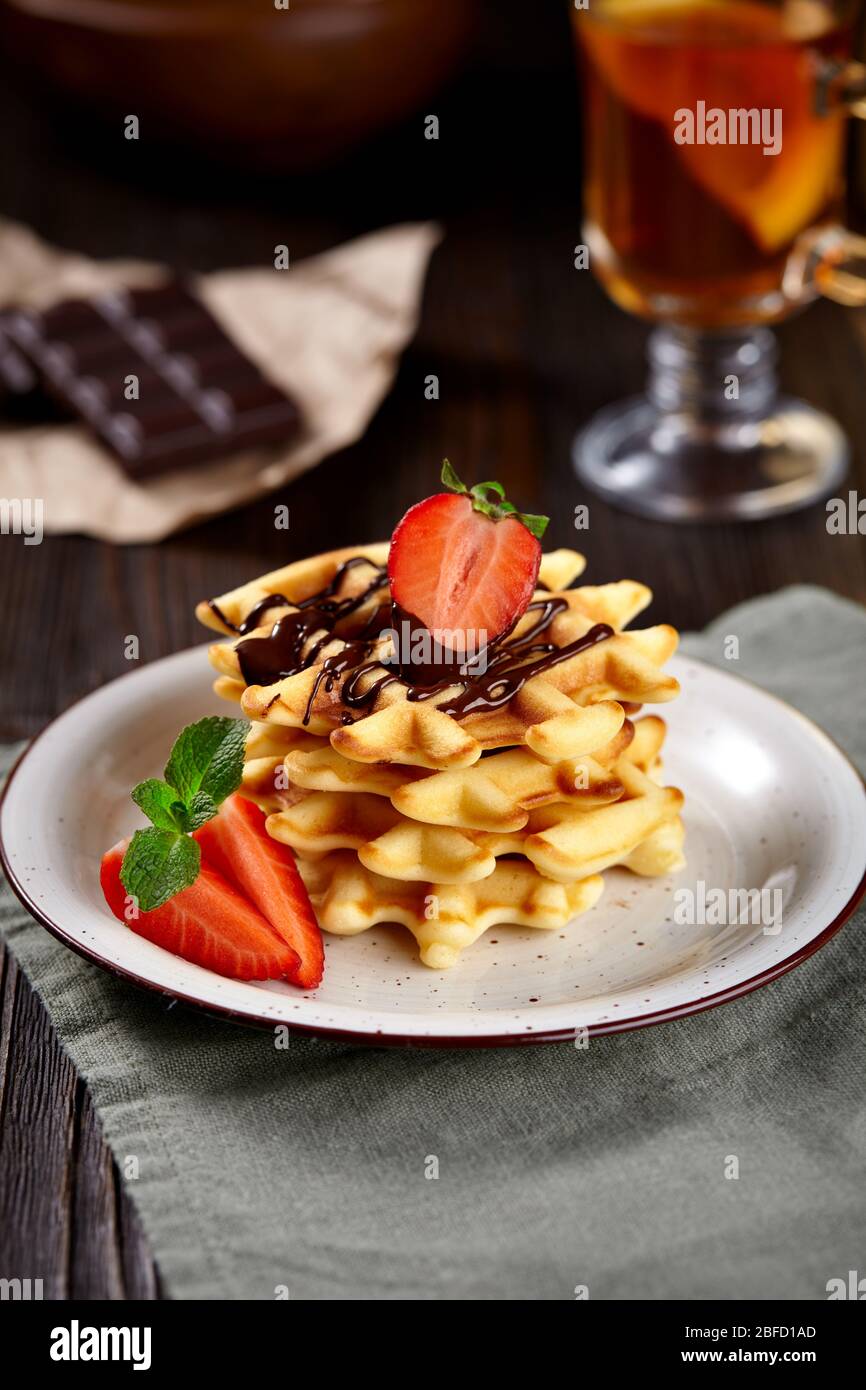 Wunderschönes Frühstück. Hausgemachte belgische Wiener Waffeln mit Schokolade und Erdbeeren, Tee auf dunklem Holzhintergrund dekoriert. Stockfoto