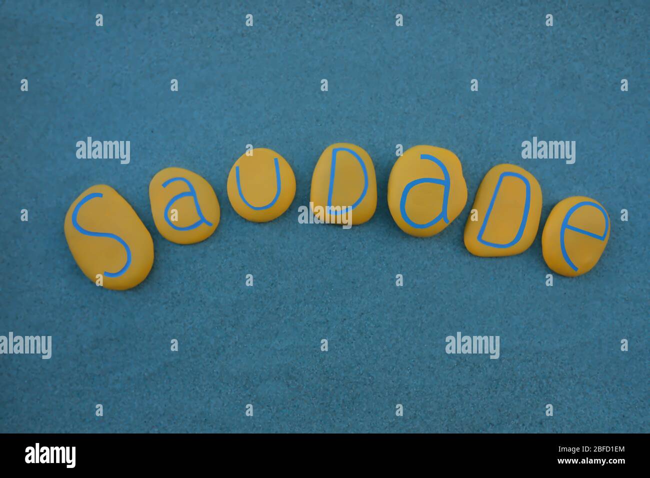 Saudade, portugiesisches Wort, das Nostalgie oder Sehnsucht bedeutet, komponiert mit gelben Steinbuchstaben über grünem Sand Stockfoto