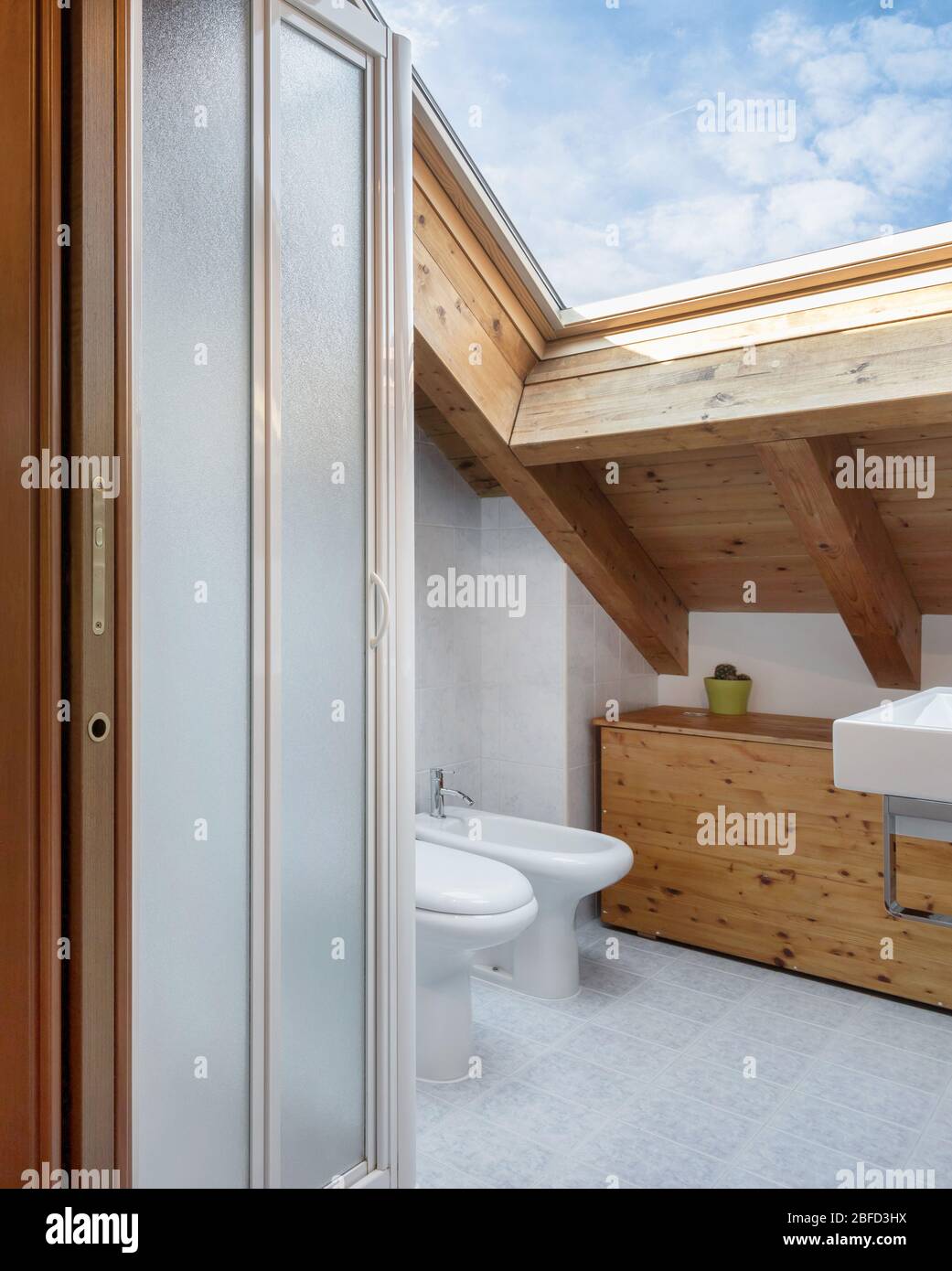 Praktisches, gemütliches Badezimmer mit Toilette, Schrank und Waschbecken. Dach mit freiliegenden Holzbalken und Dachfenster. Stockfoto