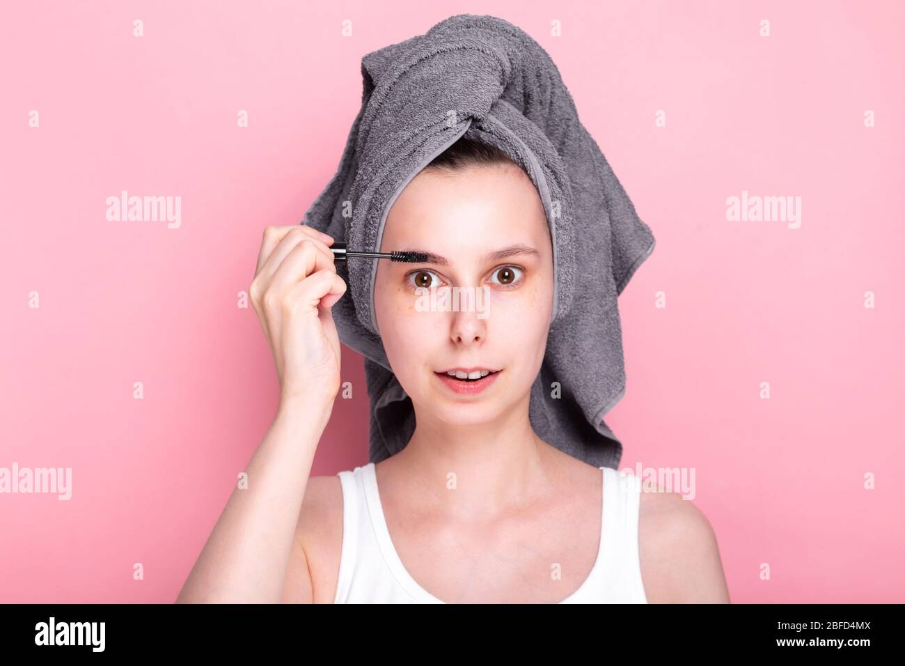 Junge Frau mit Handtuch auf dem Kopf malt ihre Augenbrauen auf sich. Konzept Spa Tag zu Hause und in Quarantäne Stockfoto
