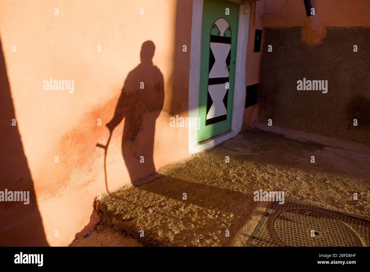 Am späten Nachmittag Schatten eines Mannes, der mit einem Stock oder einer Krücke in Marokko läuft. Stockfoto