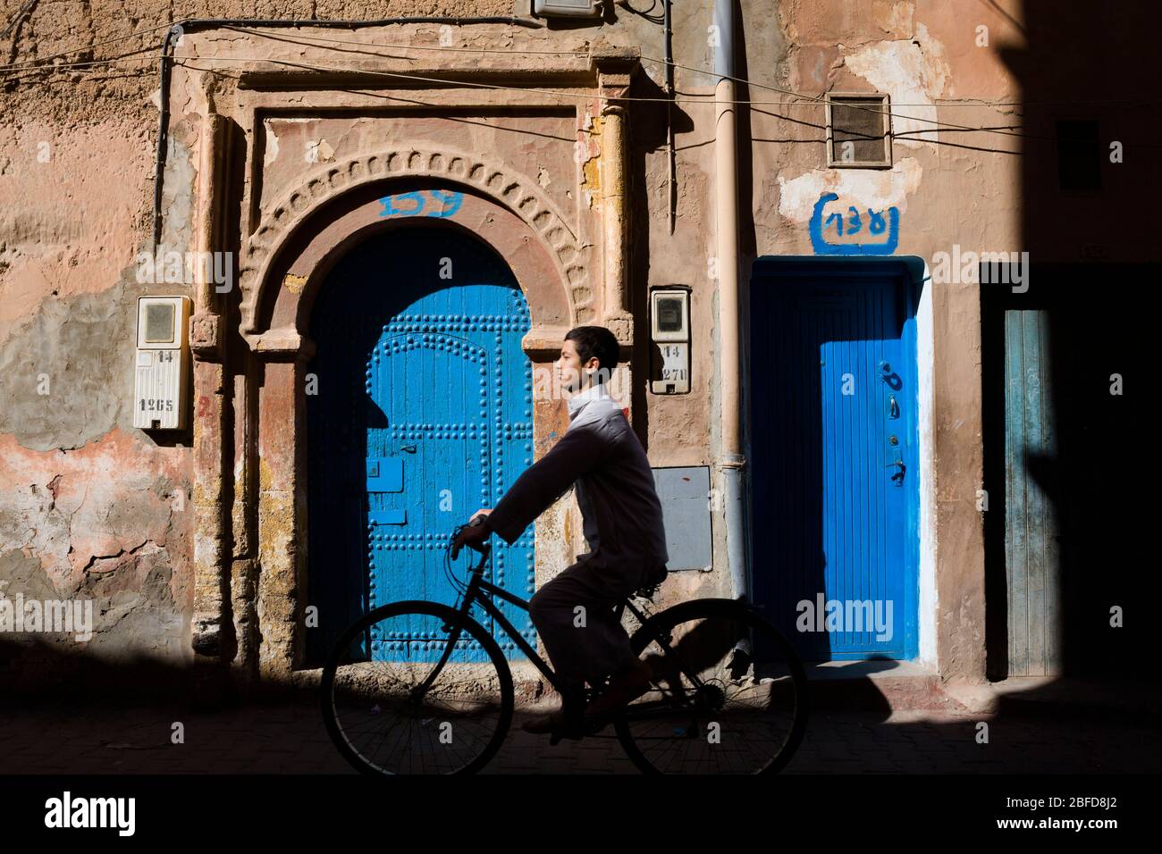 Ein lokaler Radfahrer kommt an einer verzierten türkisfarbenen Tür in der Westsahara, Marokko vorbei. Stockfoto