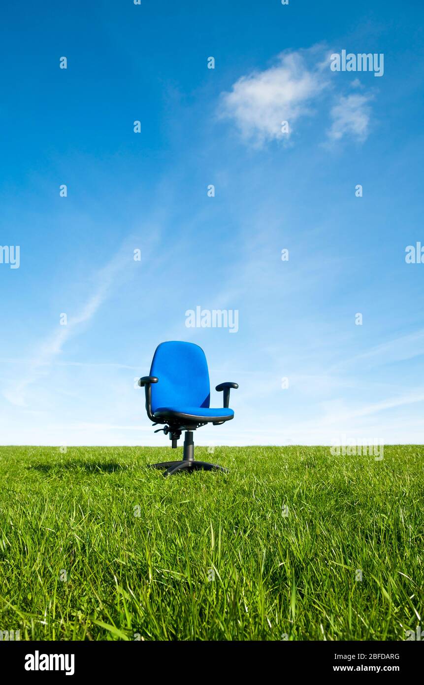 Leerer blauer Stoff Bürostuhl im Freien in der Mitte eines leeren grünen Feldes unter sonnigen blauen Himmel stehen Stockfoto