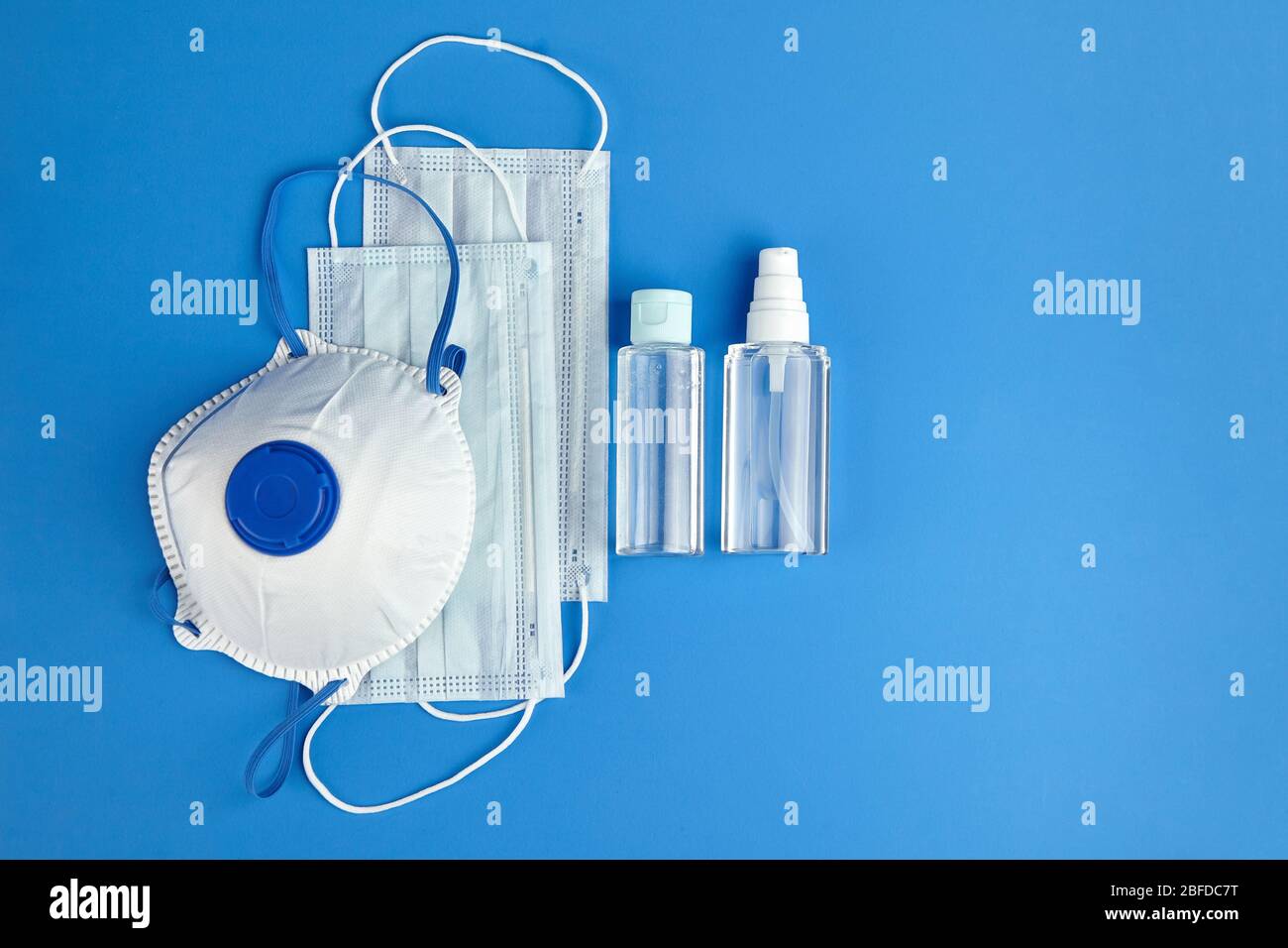 Antibakterielle Händedesinfektionsmittel, Atemschutzmaske und chirurgische Masken auf blauem Hintergrund, Draufsicht. Anti Staub atmungsaktive Einweg-Gesichtsmasken. Schutz wieder Stockfoto