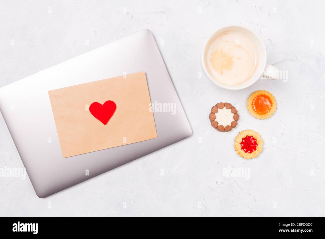 Draufsicht auf geschlossenen Laptop mit Handwerk Umschlag und roten Herzen, Tasse Kaffee und kommen Cookies. Desktop. Liebe Pflege St. Valentinstag Muttertag Stockfoto