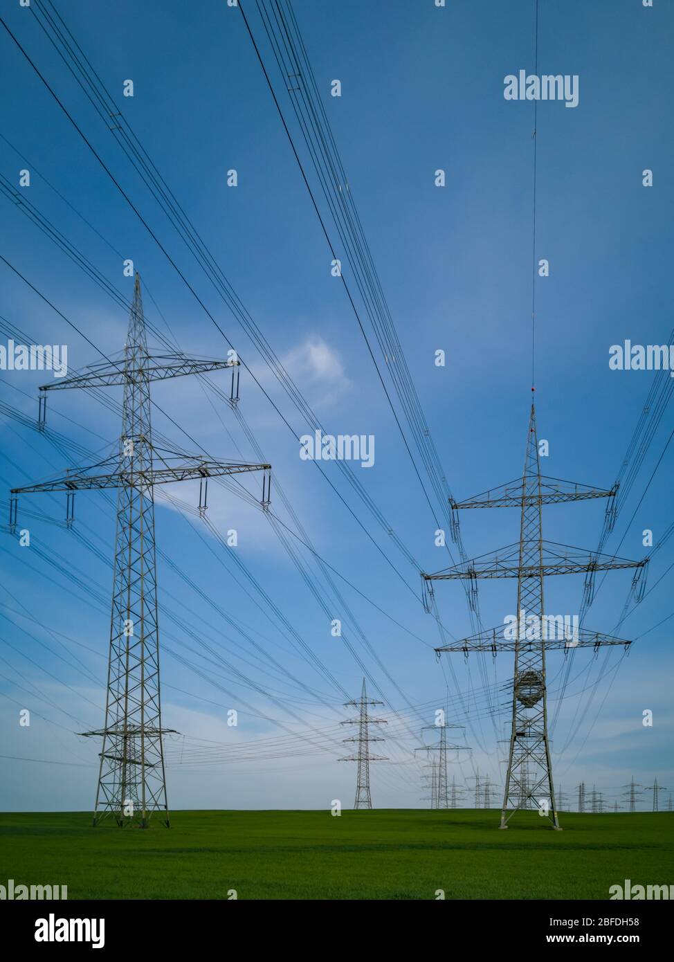 Pylone von Hochspannungsleitungen vor einem blauen Himmel mit Wolken auf einem grünen Feld, Elektroindustrie. Stockfoto