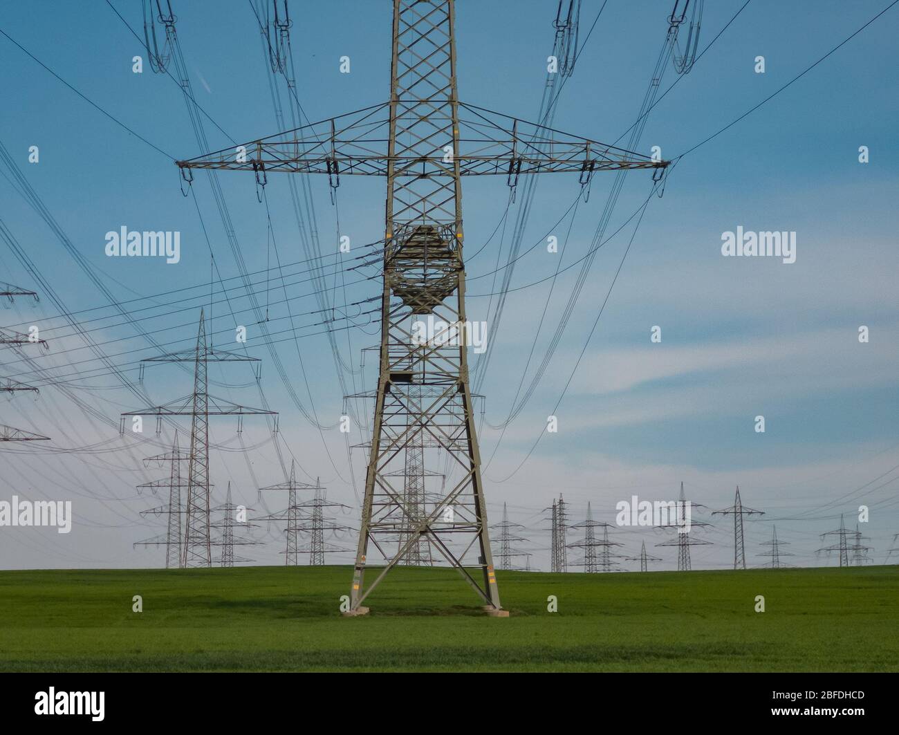 Pylone von Hochspannungsleitungen vor einem blauen Himmel mit Wolken auf einem grünen Feld, Elektroindustrie. Stockfoto