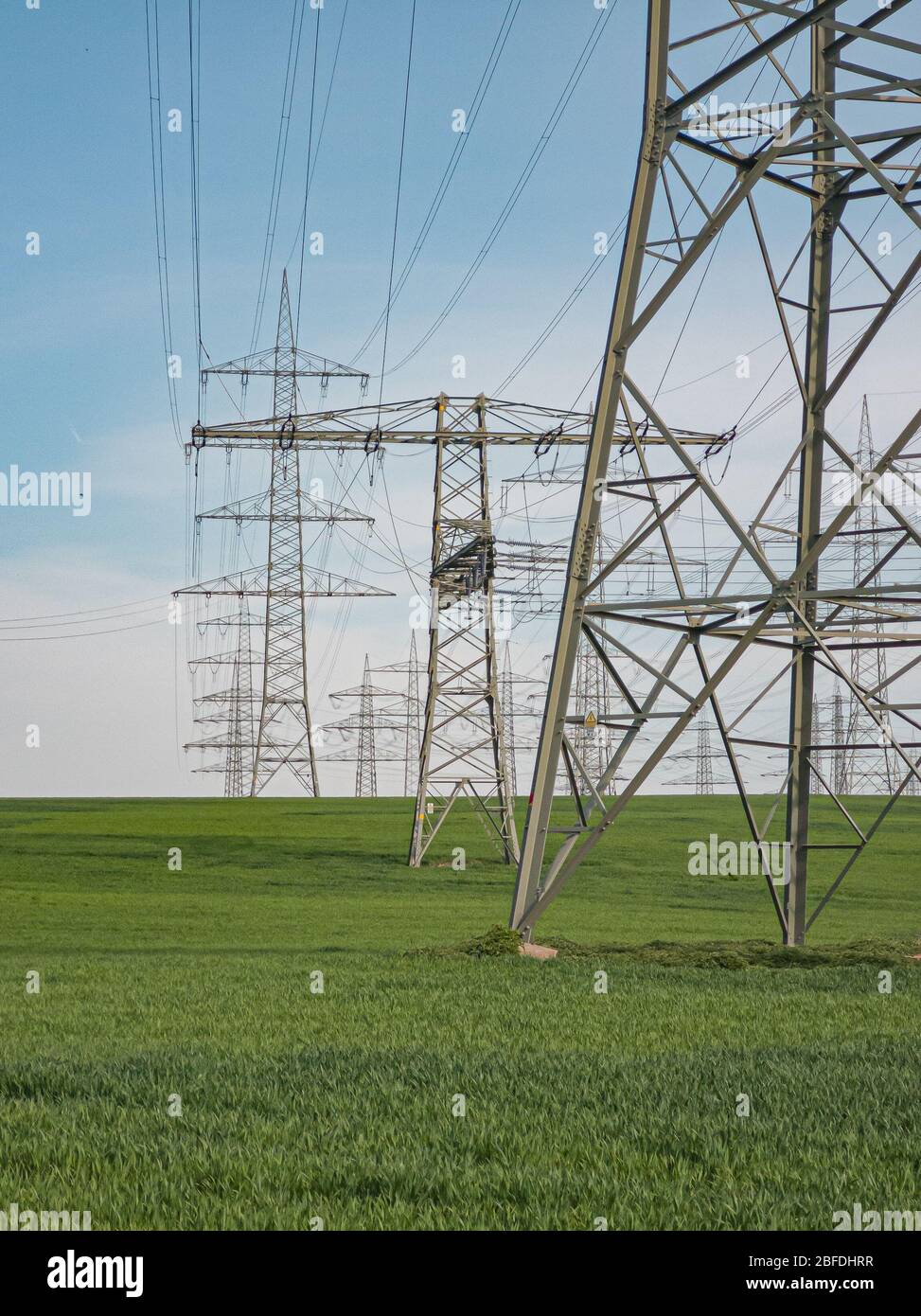 Pylone von Hochspannungsleitungen vor einem blauen Himmel mit Wolken auf einem grünen Feld, Elektroindustrie. Stockfoto