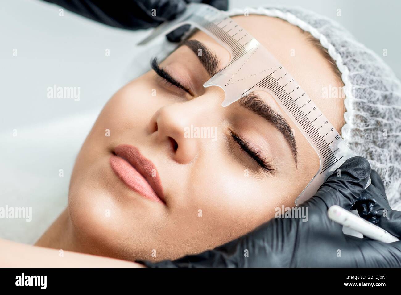 Markup mit Lineal auf Augenbrauen der jungen Frau während der dauerhaften Make-up. Stockfoto